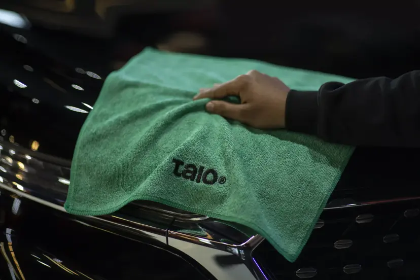 Hand wiping a dark car with a green Talo Basic towel