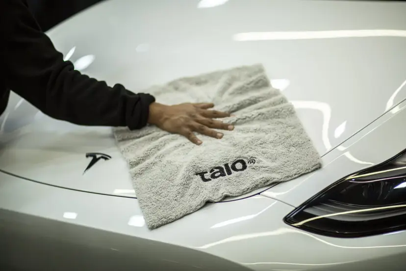 Hand drying the bonnet of a white car with a light grey Talo towel