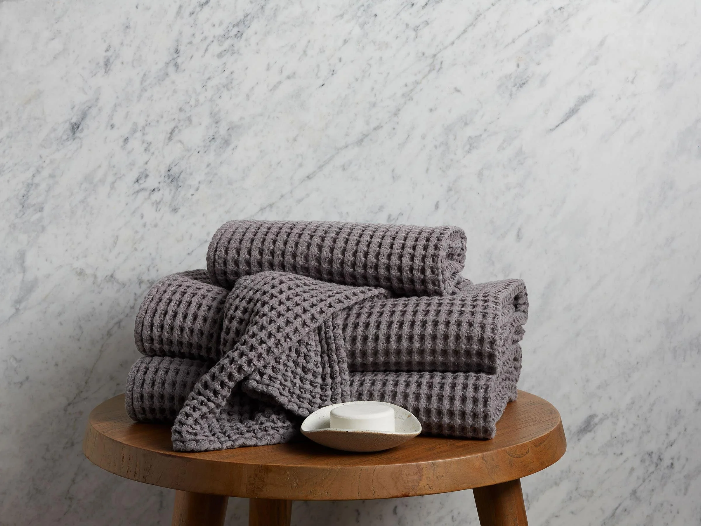 Stack of dark grey Royale Lite waffle bath towels on a wooden stool